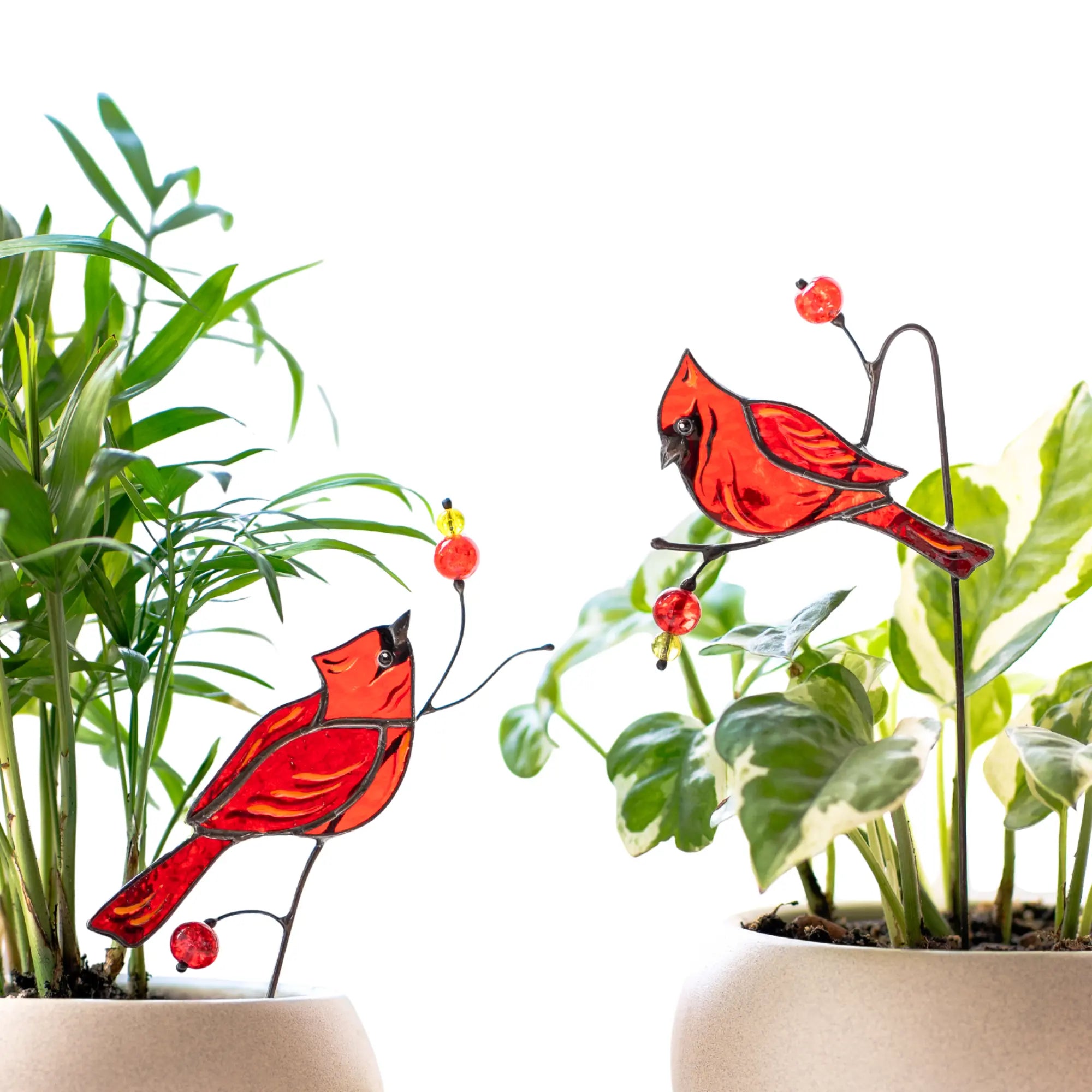 Two red cardinal bird stained glass plant stakes with green leaves in the background.