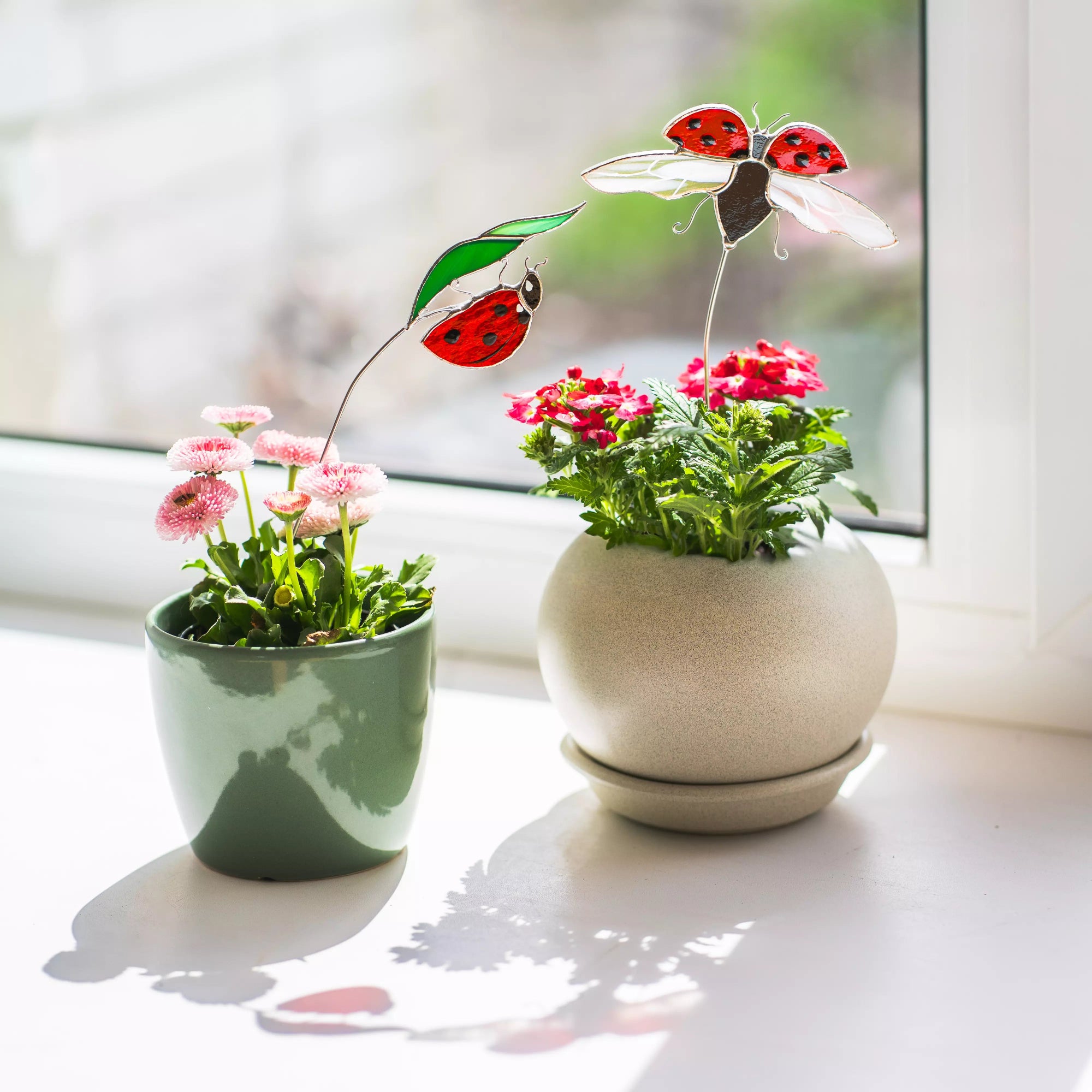 Two small potted plants with stained glass ladybug figures on a light surface.