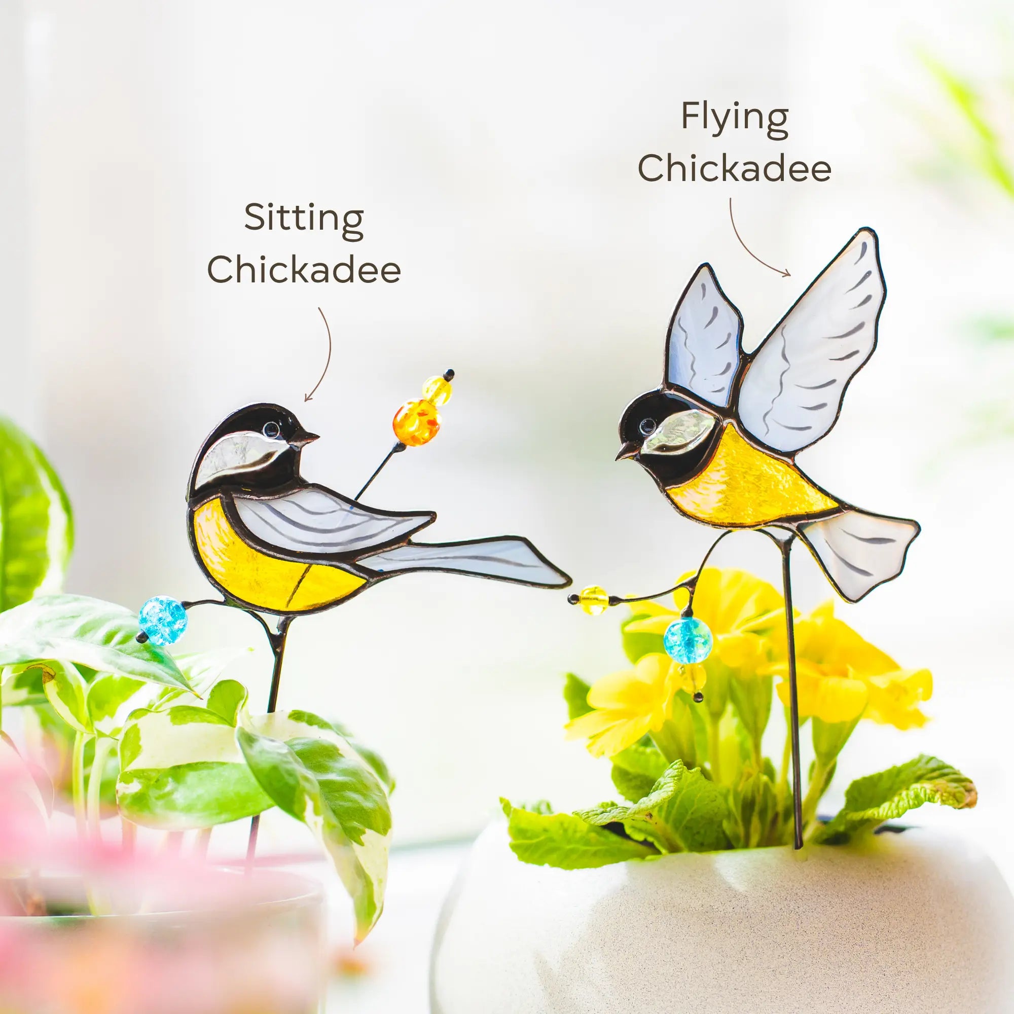 Two stained glass chickadee plant stakes, one sitting and one flying, with labels on a light background.