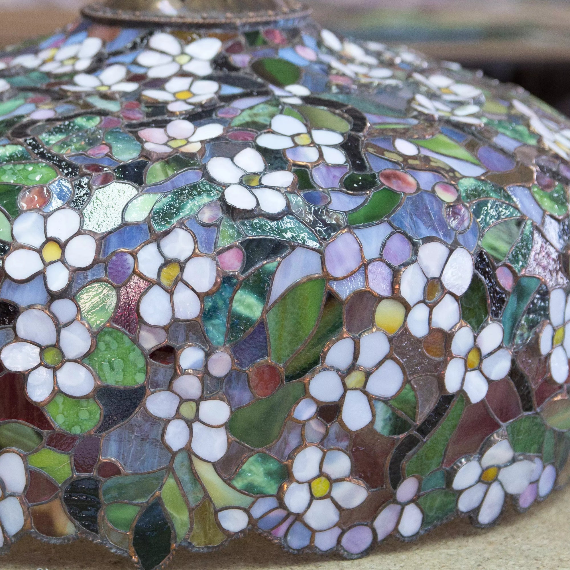 Close view of floral stained glass shade resting on a workshop table, showing detailed mosaic work.
