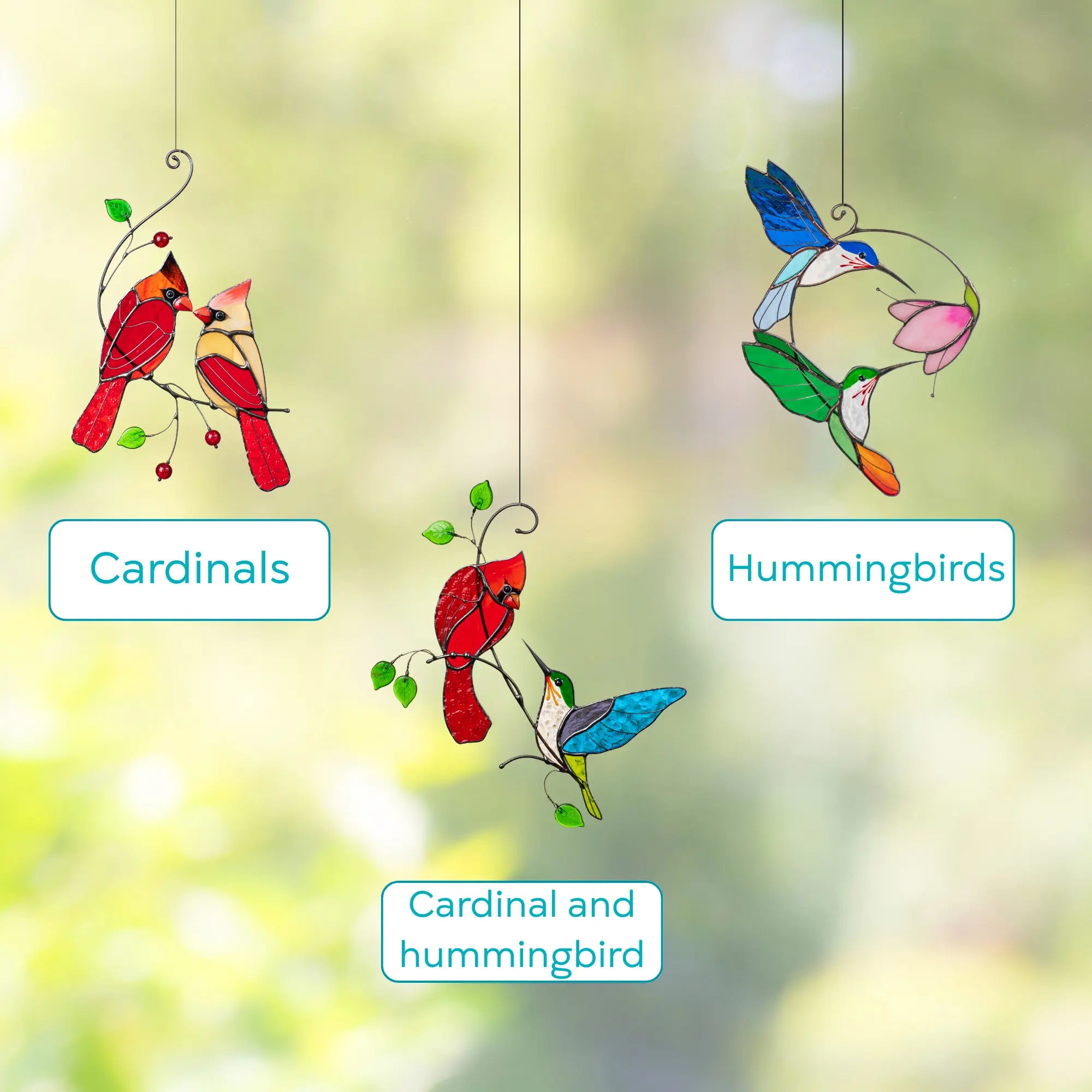 Stained glass window hangings of cardinals, hummingbirds, and a combination of both against a blurred green background.