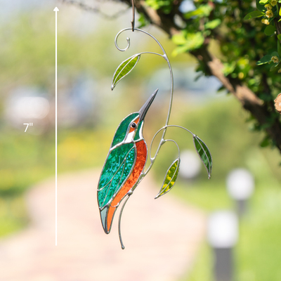 Stained glass kingfisher suncatcher measuring 7 inches, displayed outdoors with green background.