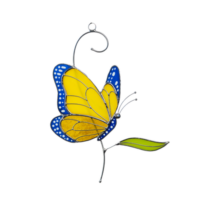 Stained glass butterfly hanging indoors, yellow and blue design with green leaf and soft light background.