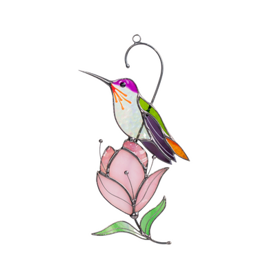 Stained glass hummingbird with purple head and green wings, perched on a soft pink magnolia flower.