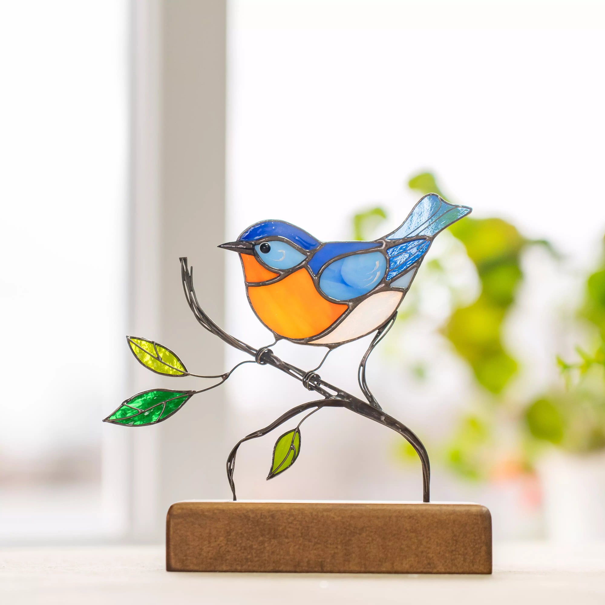 Decorative bluebird made of stained glass and wire branches, displayed on a brown wooden stand