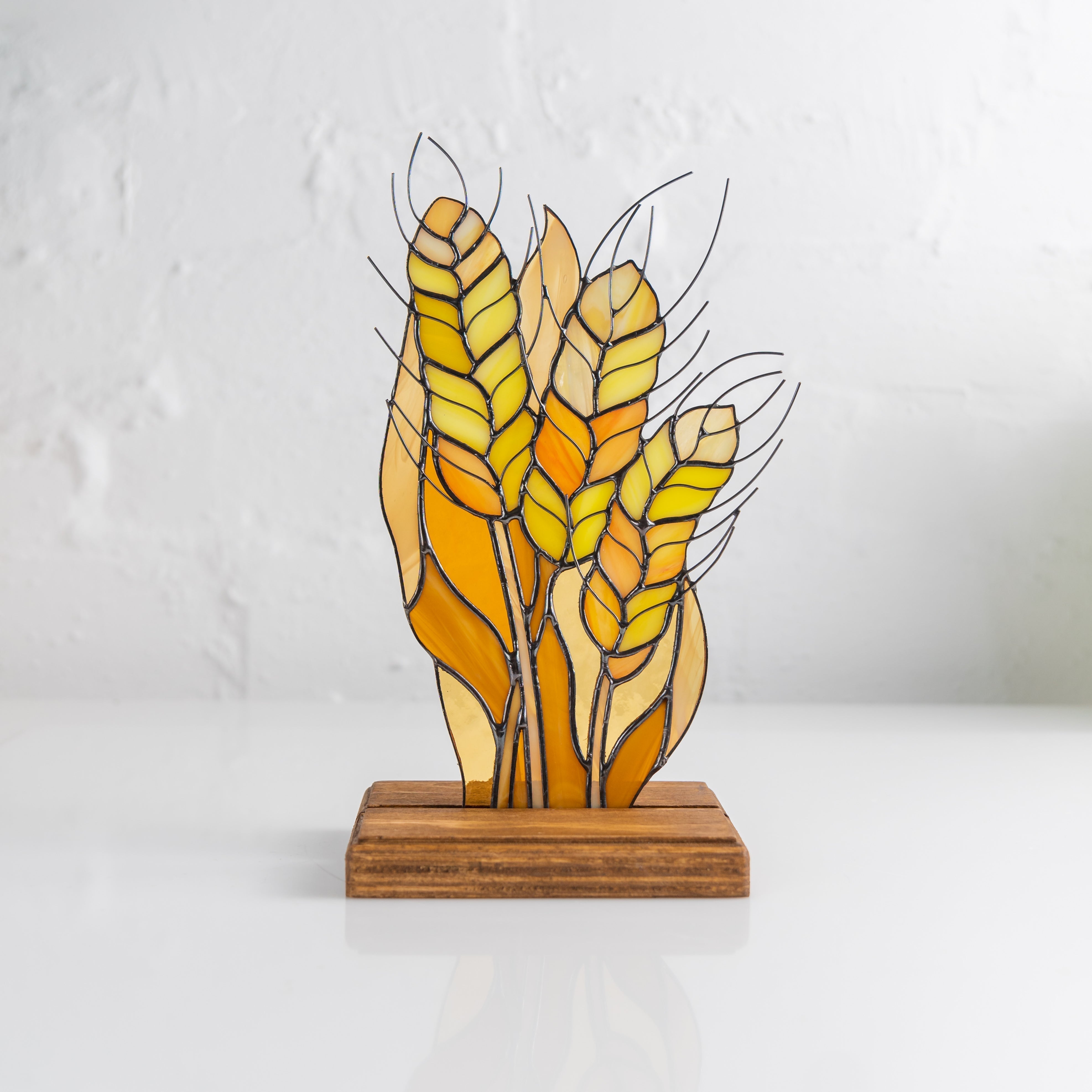 Golden yellow and orange wheat bundle crafted from stained glass with dark metal outlines on wood base.