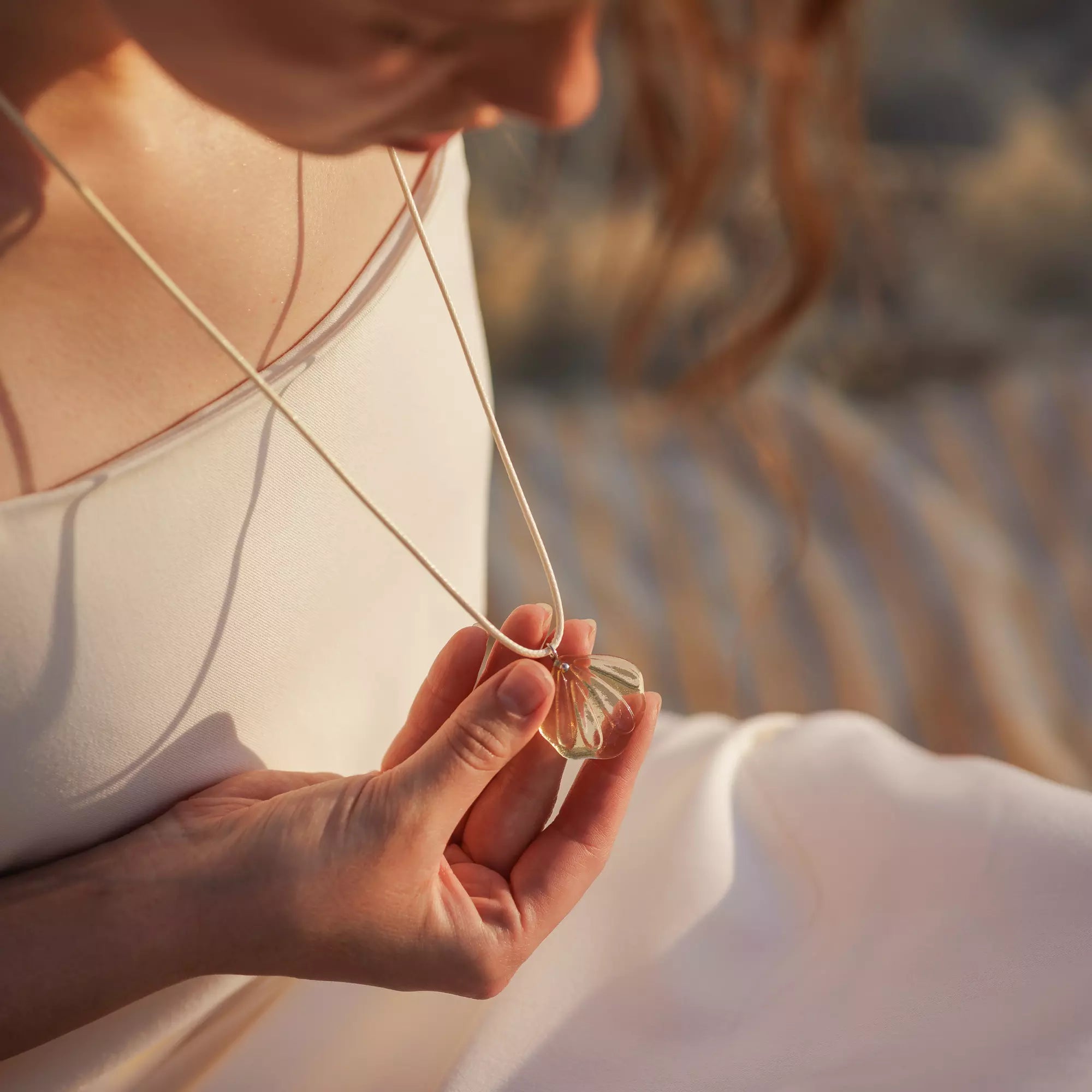 Person holding a necklace with a golden stained glass pendant against a blurred natural background