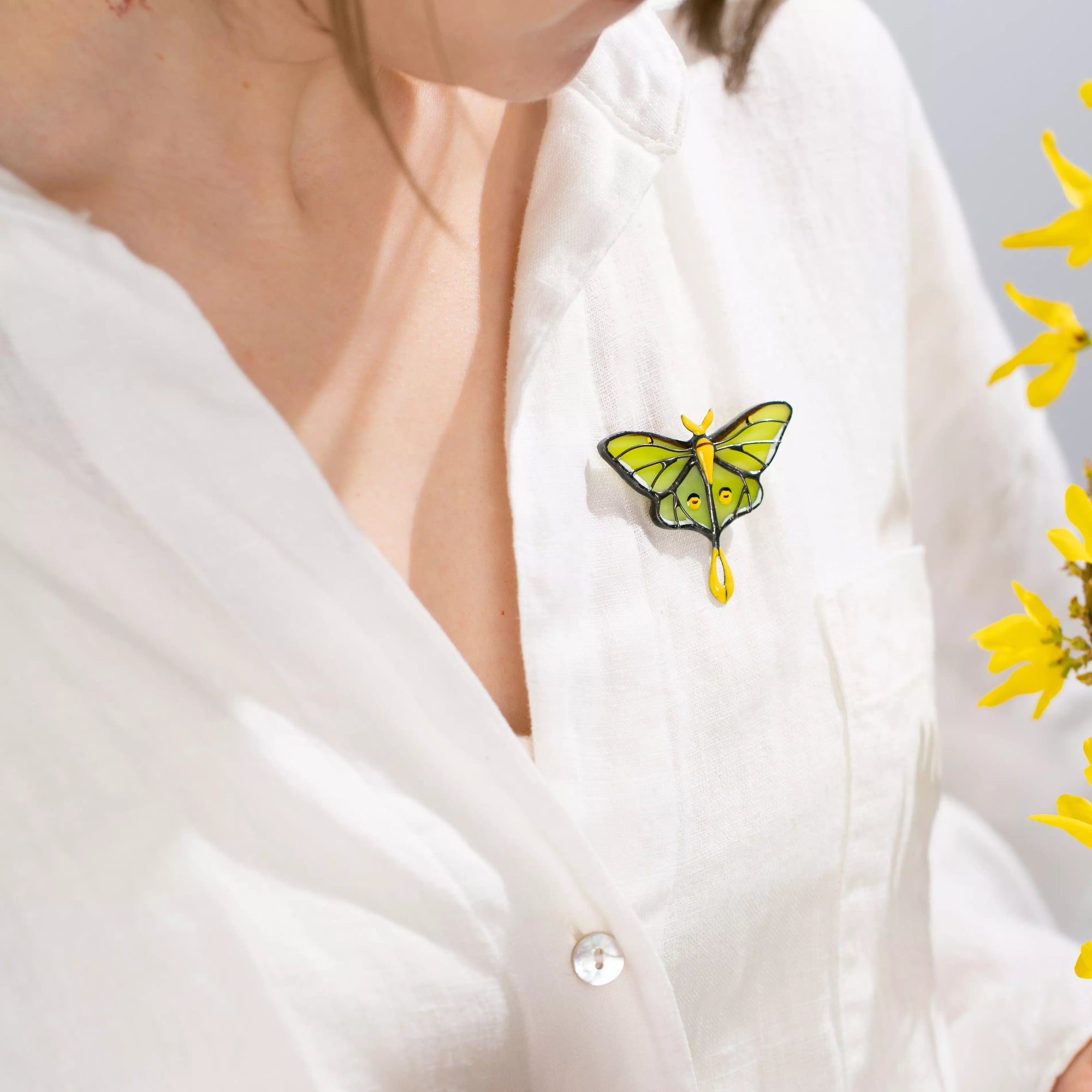 White blouse with a stained glass butterfly brooch and yellow flowers on a light gray background