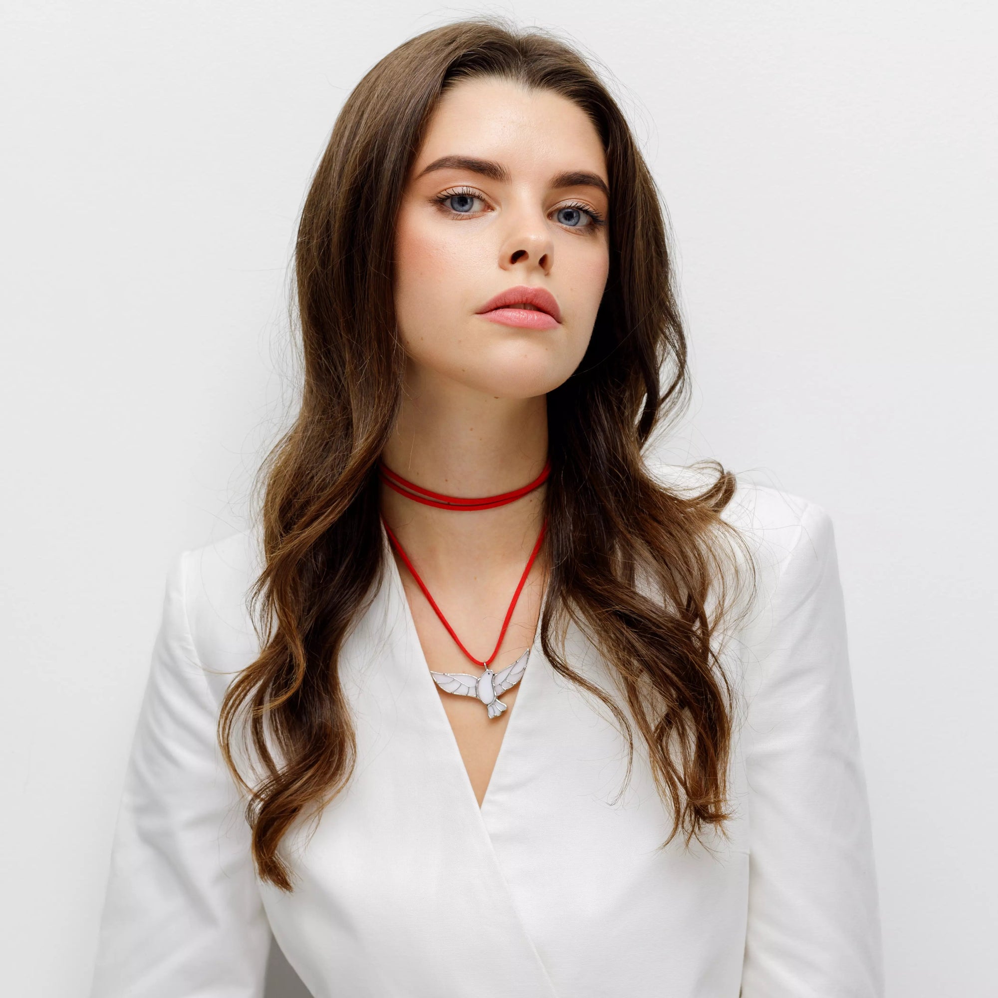 Woman in white blazer wearing a red cord necklace with white stained glass dove pendant
