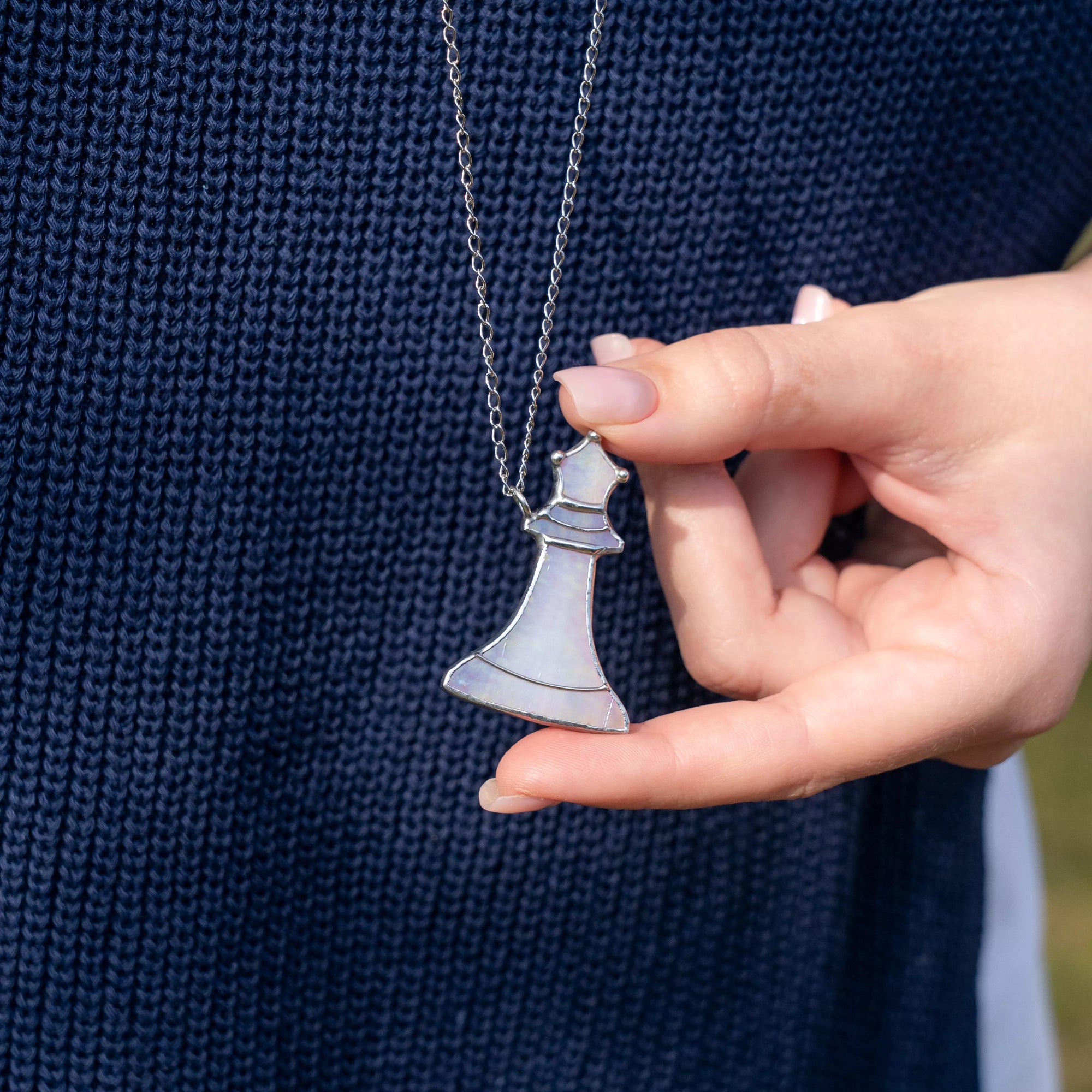 Model holding stained glass queen necklace outdoors, showcasing scale and elegance of pendant in natural light.