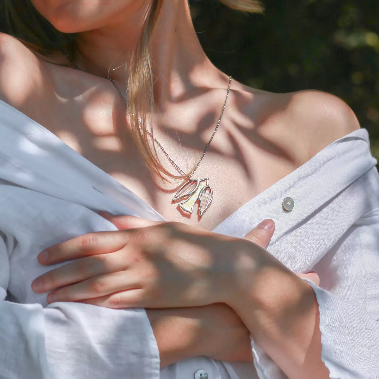 Stained glass bird pendant on a necklace, partially covered by a white shirt.