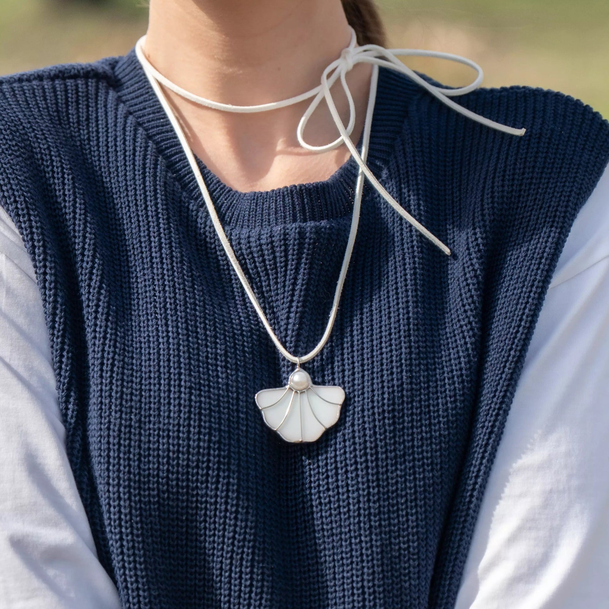 Elegant stained glass shell necklace with pearl center, styled with a bow-tied white suede cord – a fresh accessory for warm weather.	