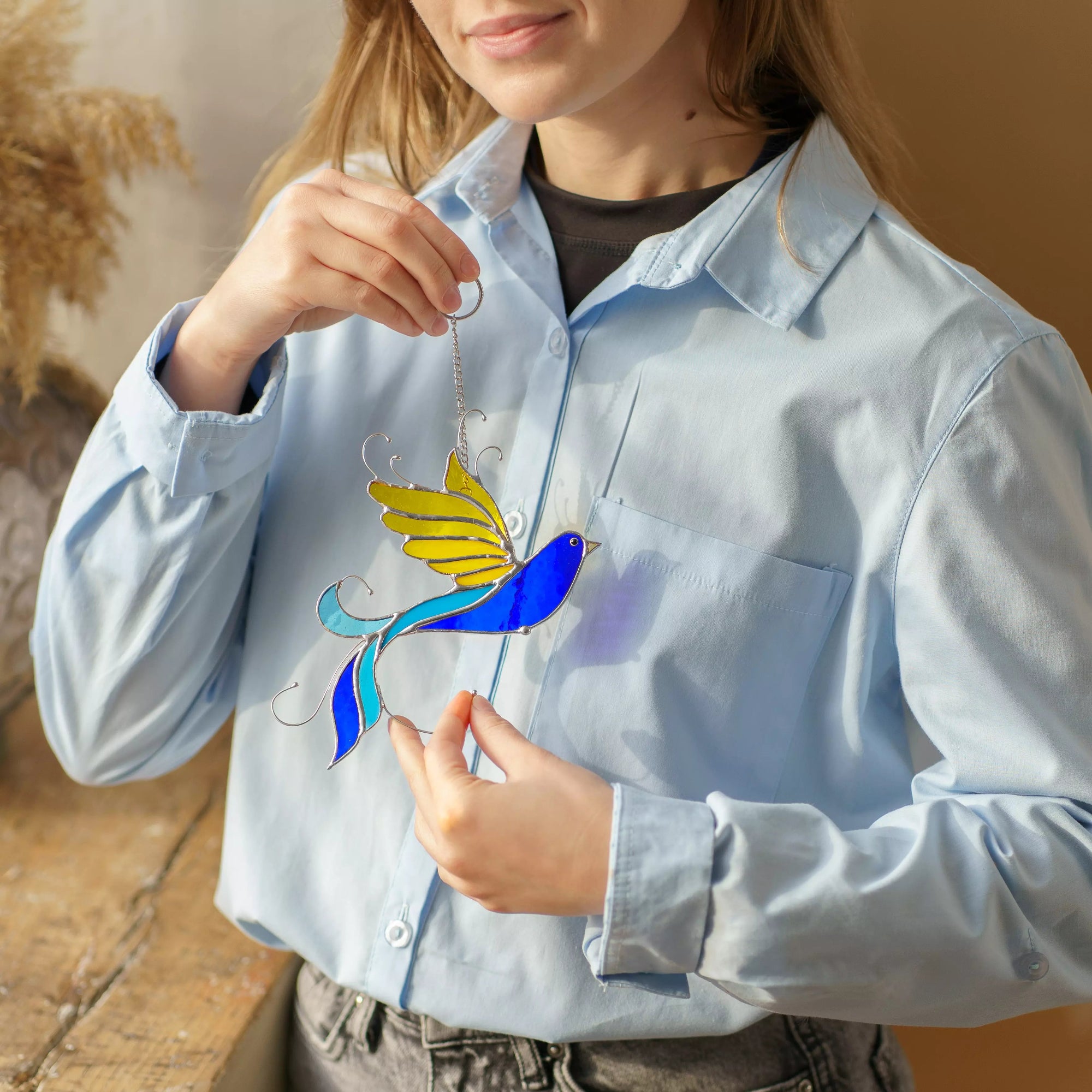 Women holds in hands stained glass suncatcher  bird that casts a soft shadow on a shirt