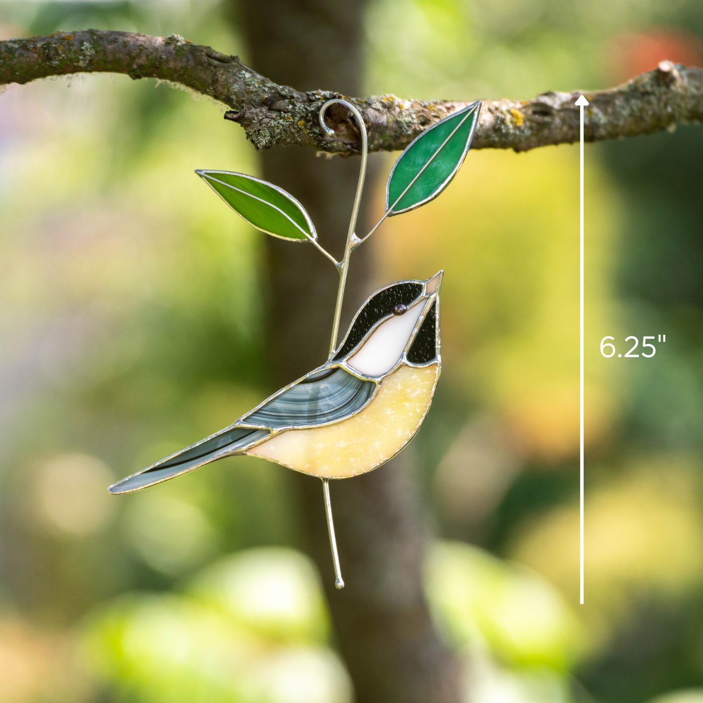 Stained glass chickadee with yellow belly and gray wing, hanging from a branch with green leaves and marked as 6.25 inches tall.