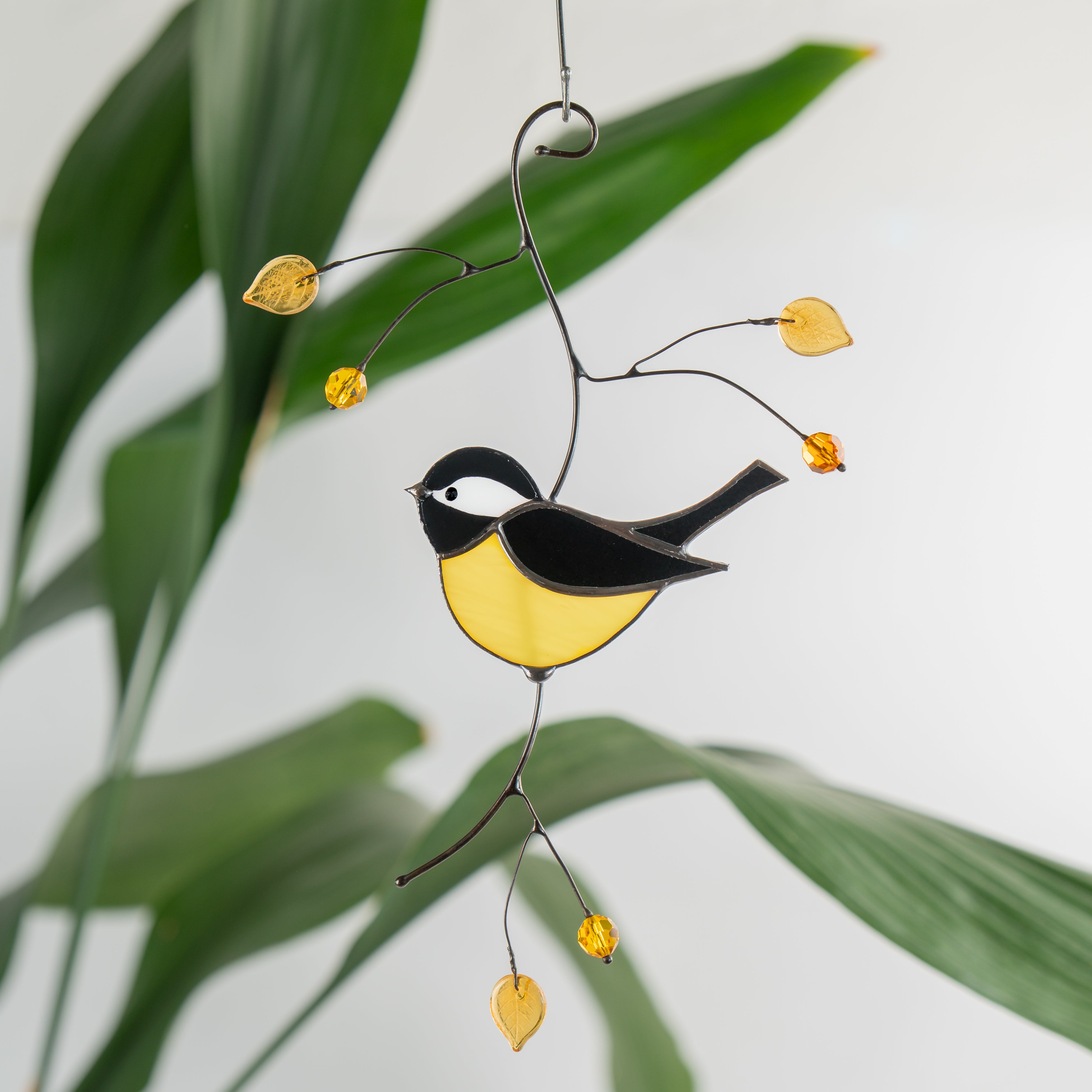 Stained glass chickadee suncatcher with yellow leaves and orange beads hanging in front of green plants