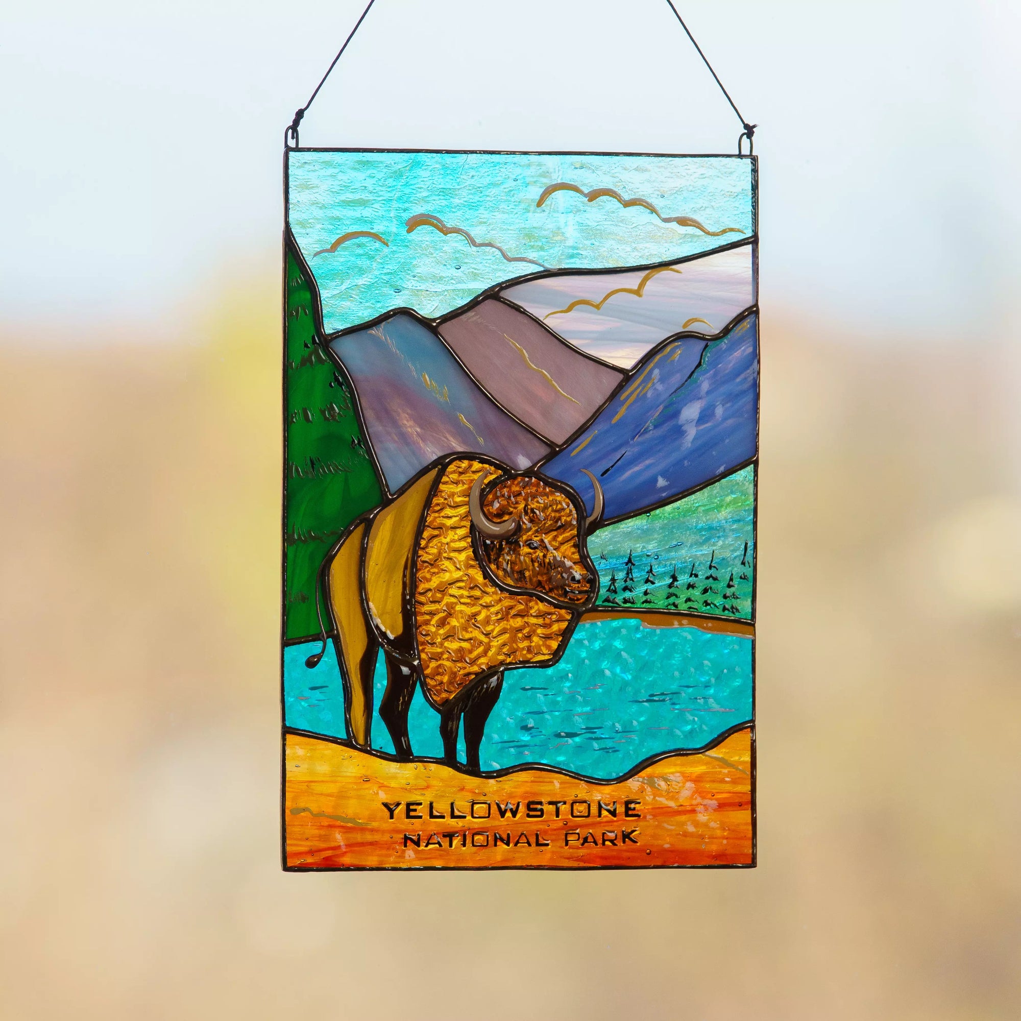 Stained glass panel of a bison in Yellowstone National Park with mountains and water in the background.
