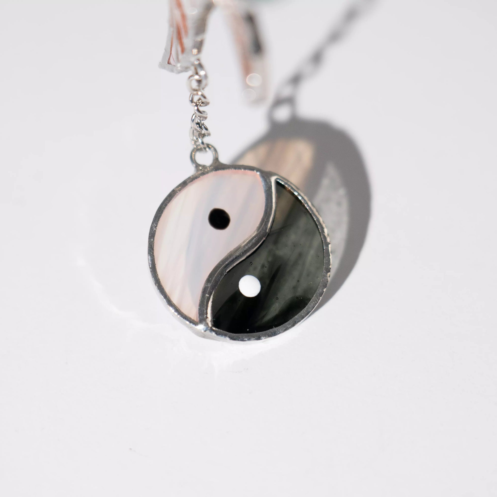 Yin yang stained glass pendant on a chain against a light gray background