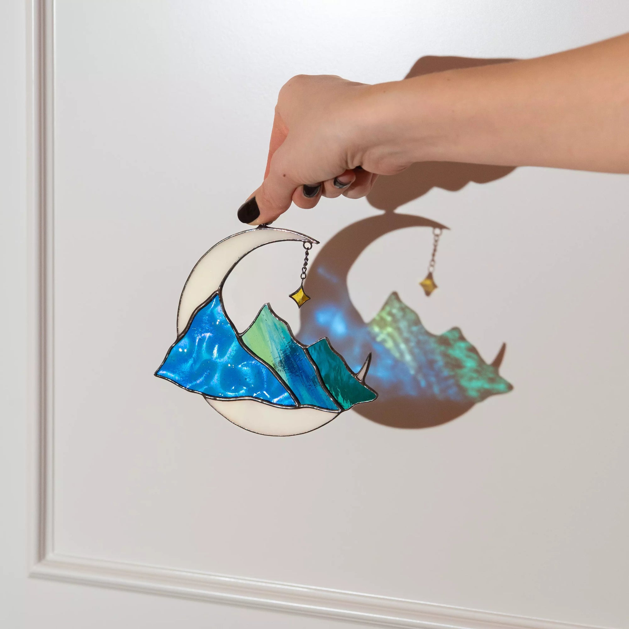 hand holding stained glass moon with mountains celestial suncatcher