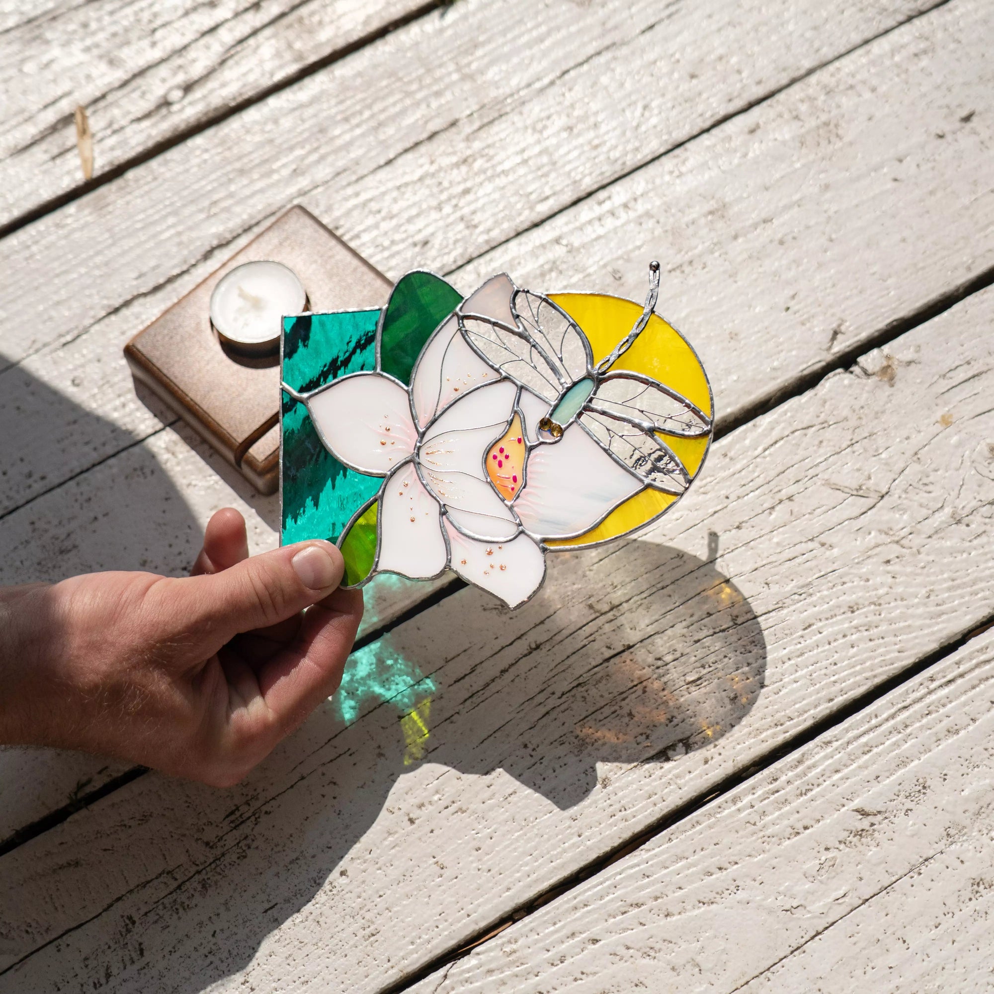 Hand holding a stained glass panel with floral and dragonfly design on wooden surface