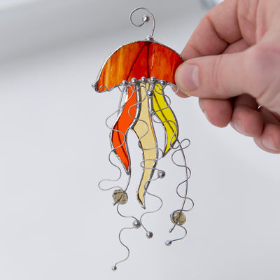 Stained glass window hanging of an orange jellyfish with yellow tentacles