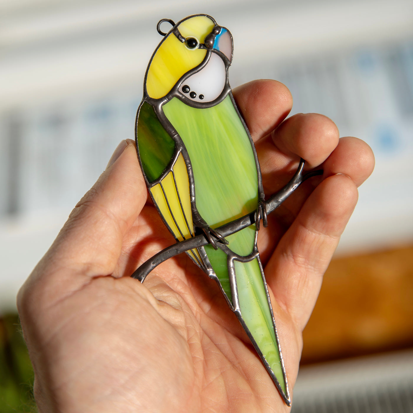 Suncatcher of a stained glass green budgie sitting on the branch
