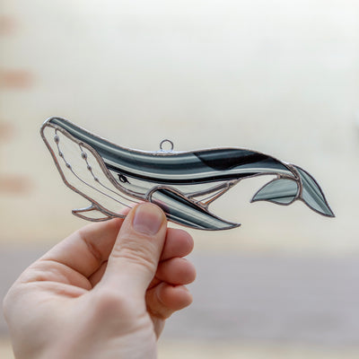 Stained glass window hanging of a black with blotchiness whale with clear lower part