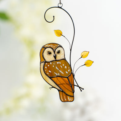 Stained glass owl in warm brown tones with yellow glass leaves, hanging in a softly lit interior