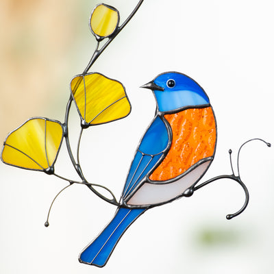 Close-up of stained glass blue and orange bird with textured yellow flowers on curved metal branches