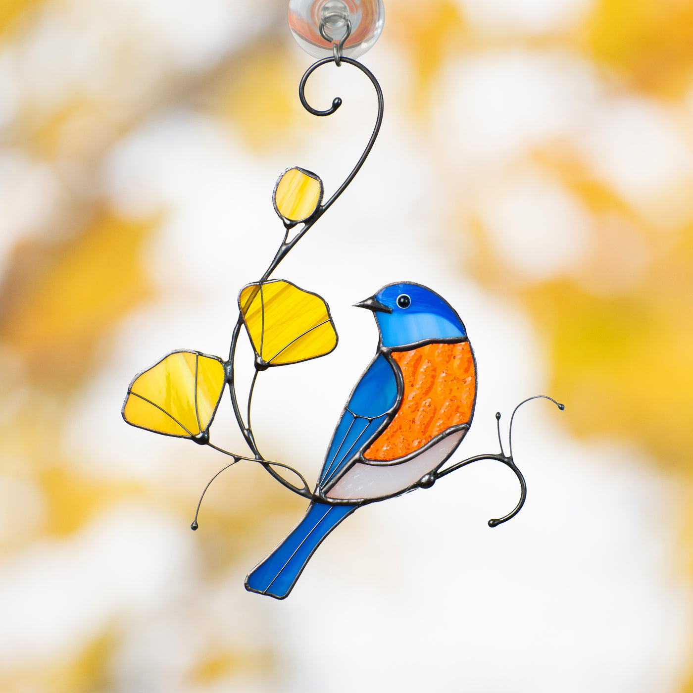 Stained glass bluebird with orange tummy and yellow flowers, hanging on a window with autumn background