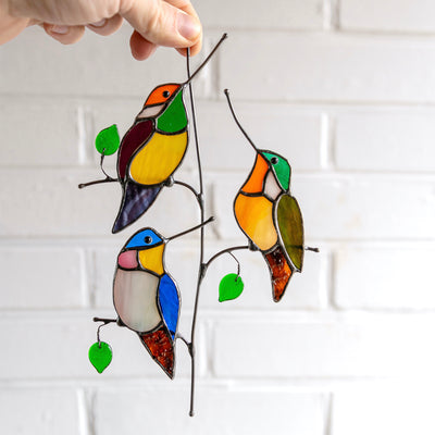 Suncatcher of three stained glass hummingbirds sitting on the vertical branch