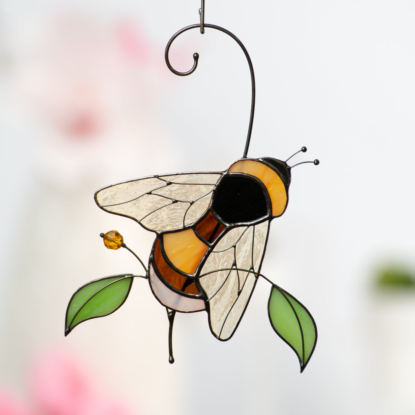 Glass bumble bee suncatcher against a soft pink and white floral background.