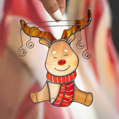 Hand holding a stained glass reindeer ornament with curly antler wires and red nose.