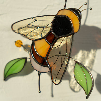 Detailed view of a glass bumble bee suncatcher with golden wings and green leaves.