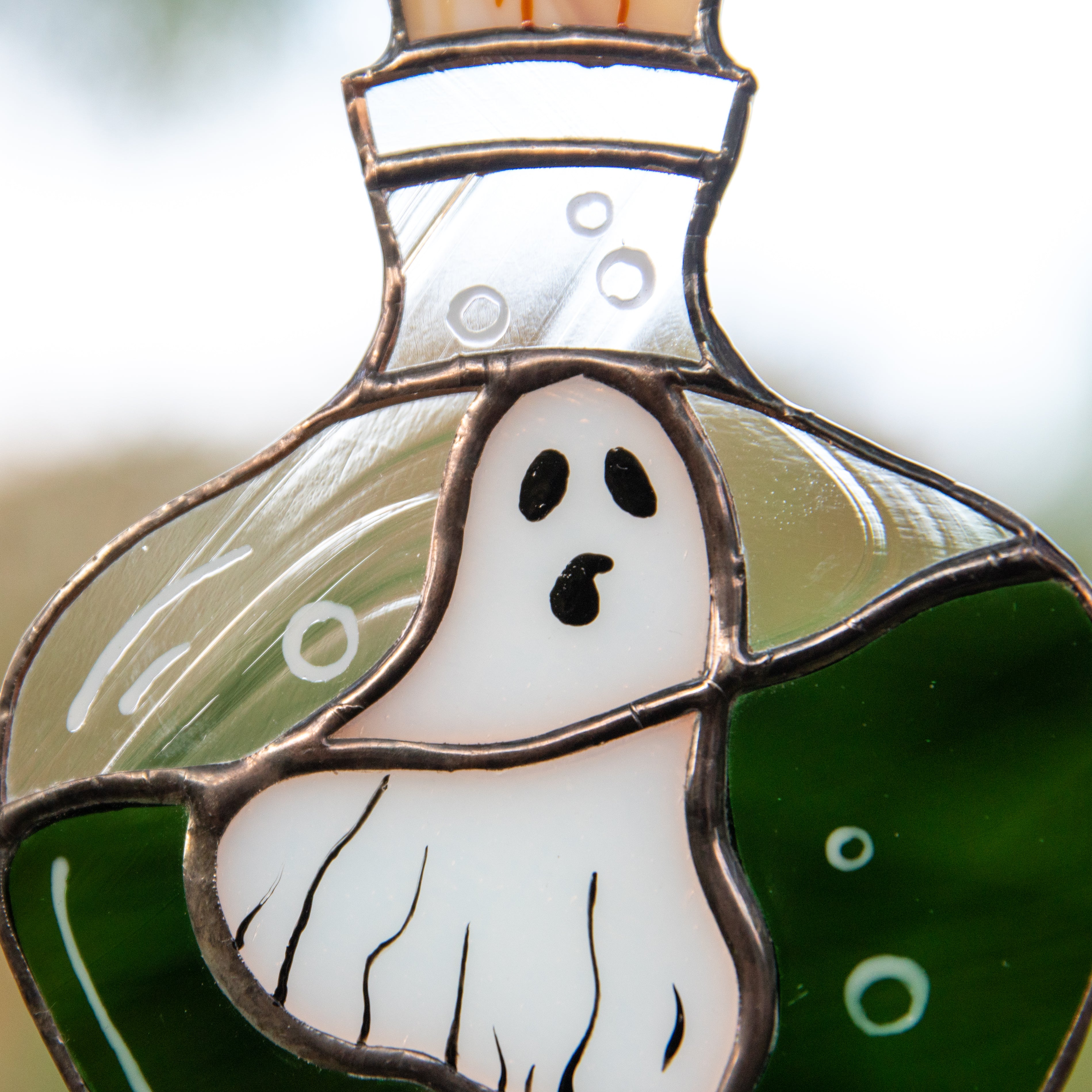 Detailed close-up of a ghost-shaped stained glass piece inside a bottle design, showing white, green, and transparent glass textures.