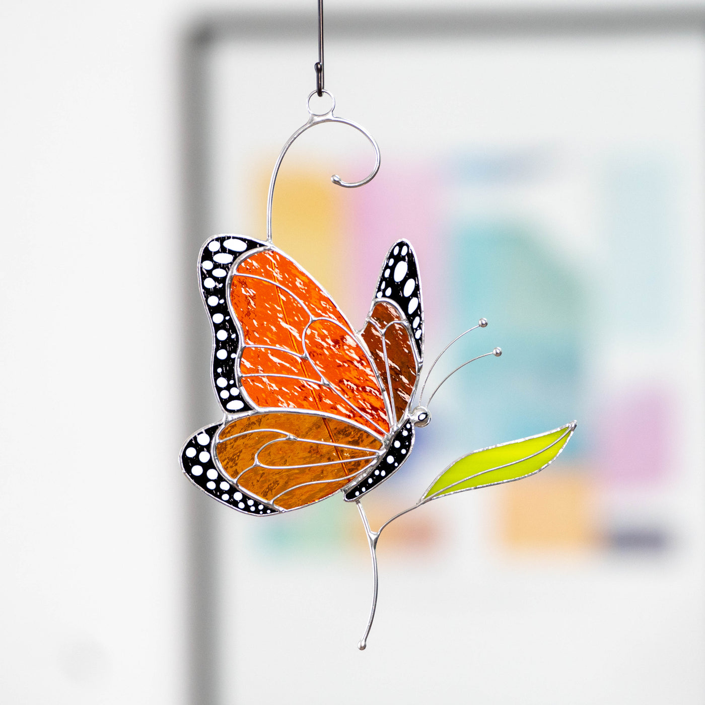 Side view stained glass monarch butterfly hanging indoors with colorful background.