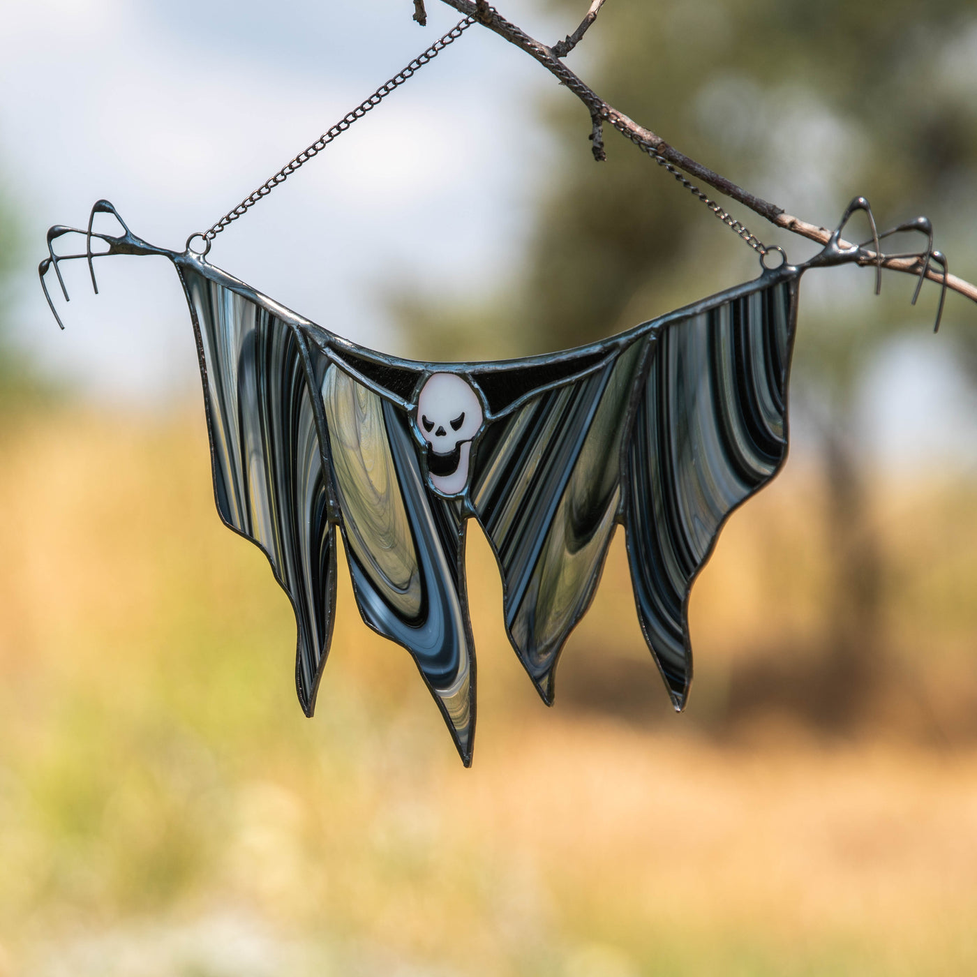 Grim Reaper glass figure with a ghostly shape and chain hanging outdoors in sunlight