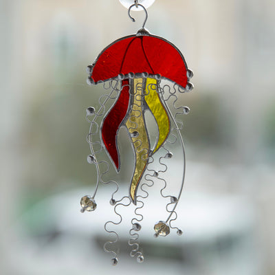 Window hanging of an orange stained glass jellyfish suncatcher with two yellow tentacles