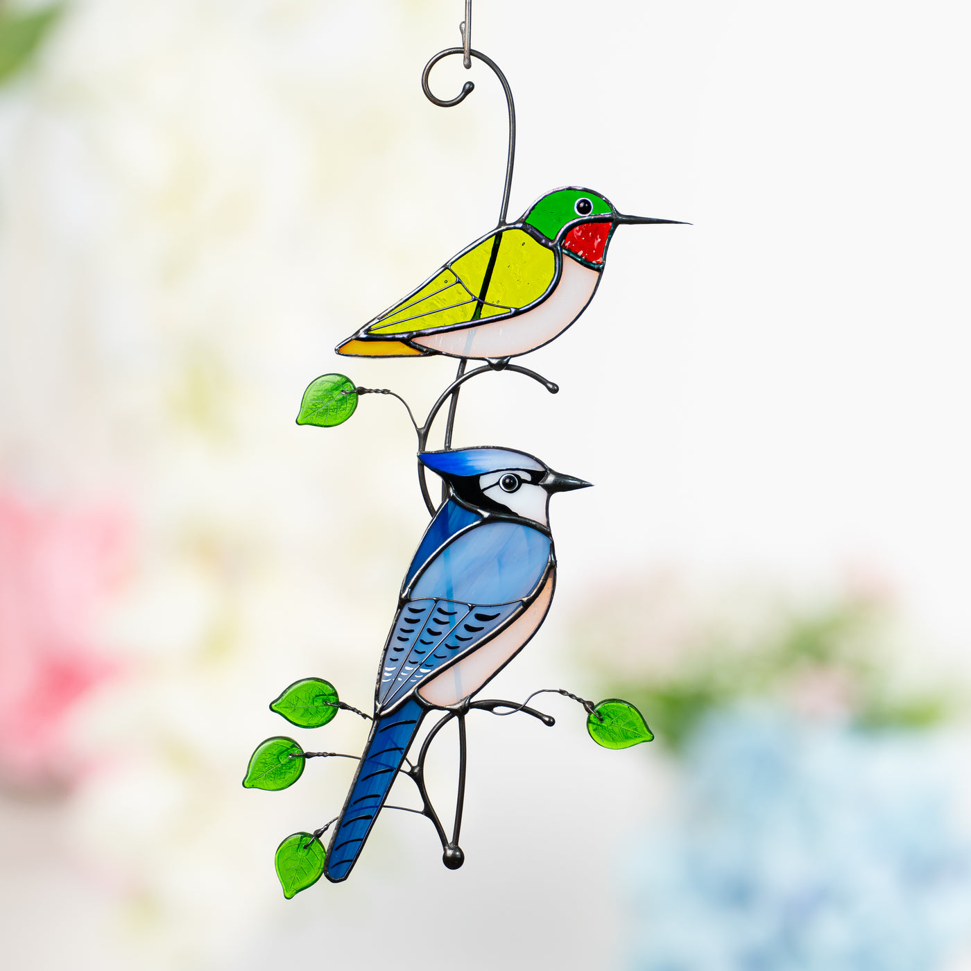 Stained glass window hanging of a green hummingbird and a bluejay below