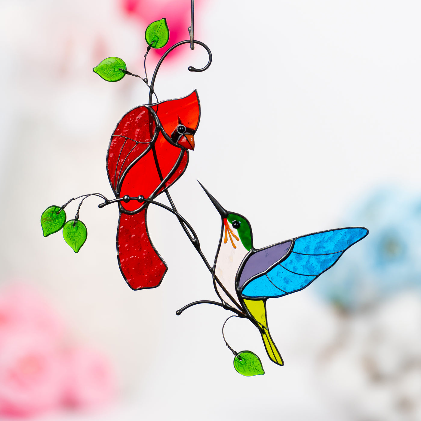 Stained glass window hanging of a red cardinal looking at multicolour hummingbird