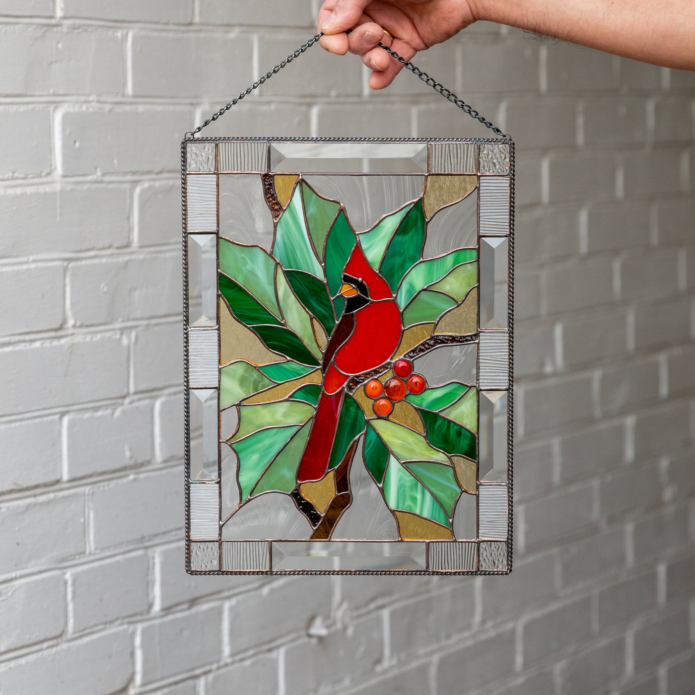 Elegant stained glass panel of a red winter bird sitting on the branch with leaves and berries