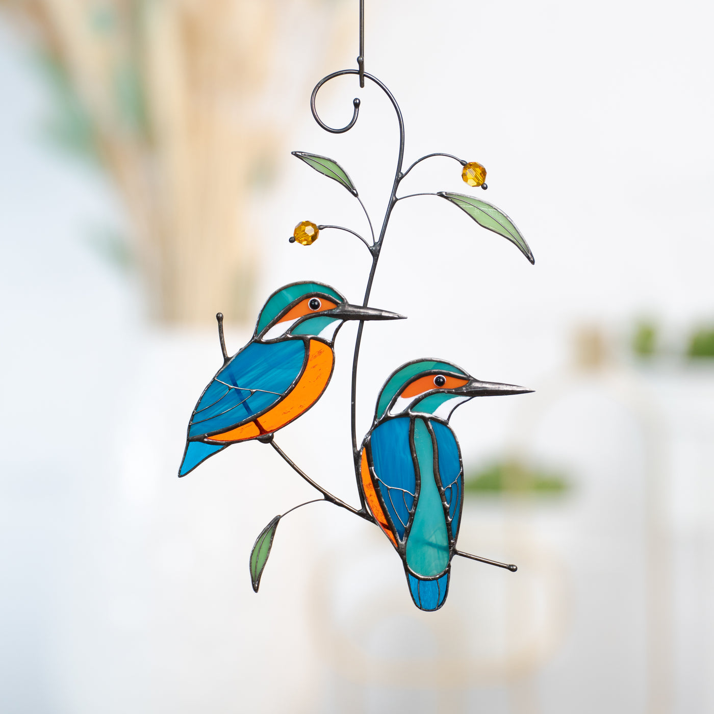 Stained glass suncatcher of two kingfishers sitting on the branch with leaves and berries 