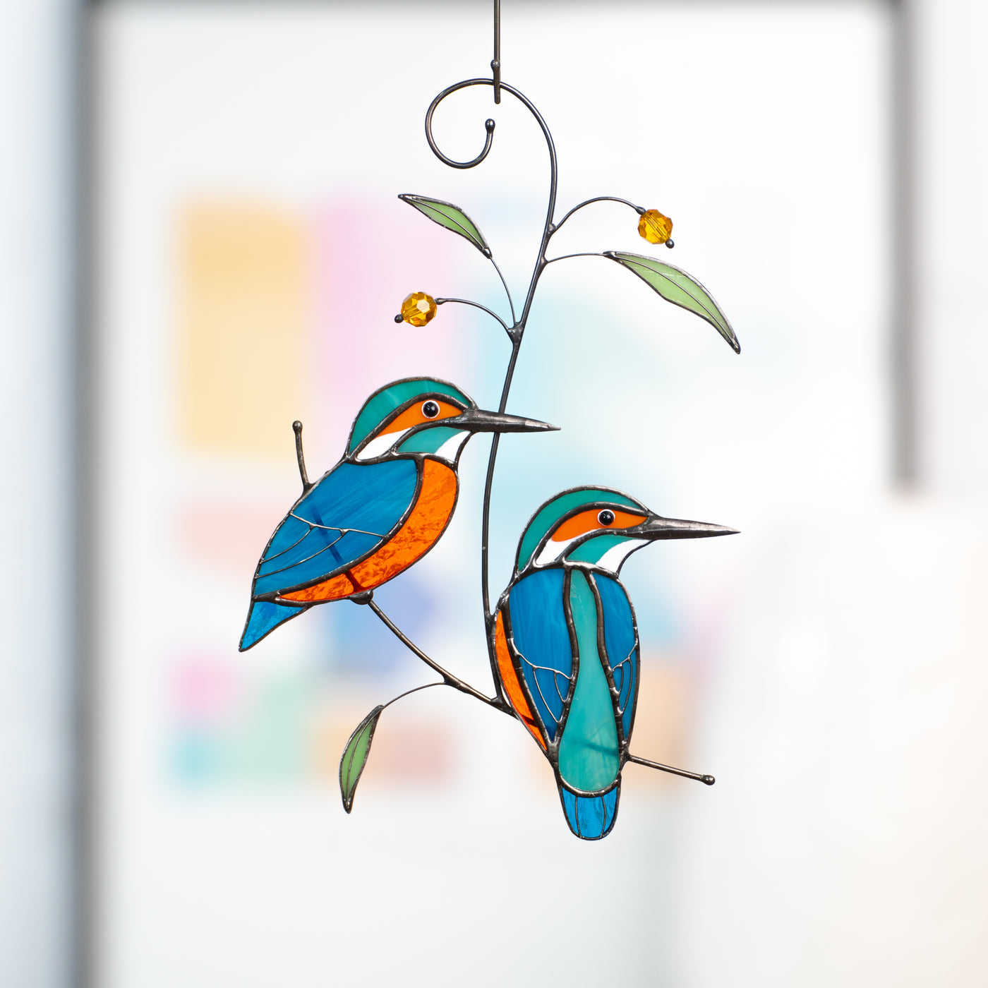 Stained glass suncatcher of two kingfishers sitting on the branch with leaves and berries 