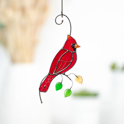 Stained glass window hanging of a red cardinal on the branch with leaves