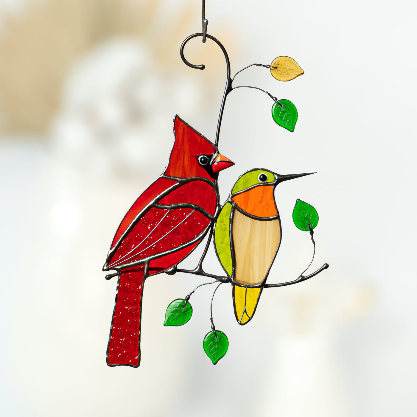 Stained glass suncatcher of a red cardinal and green hummingbird sitting on the branch