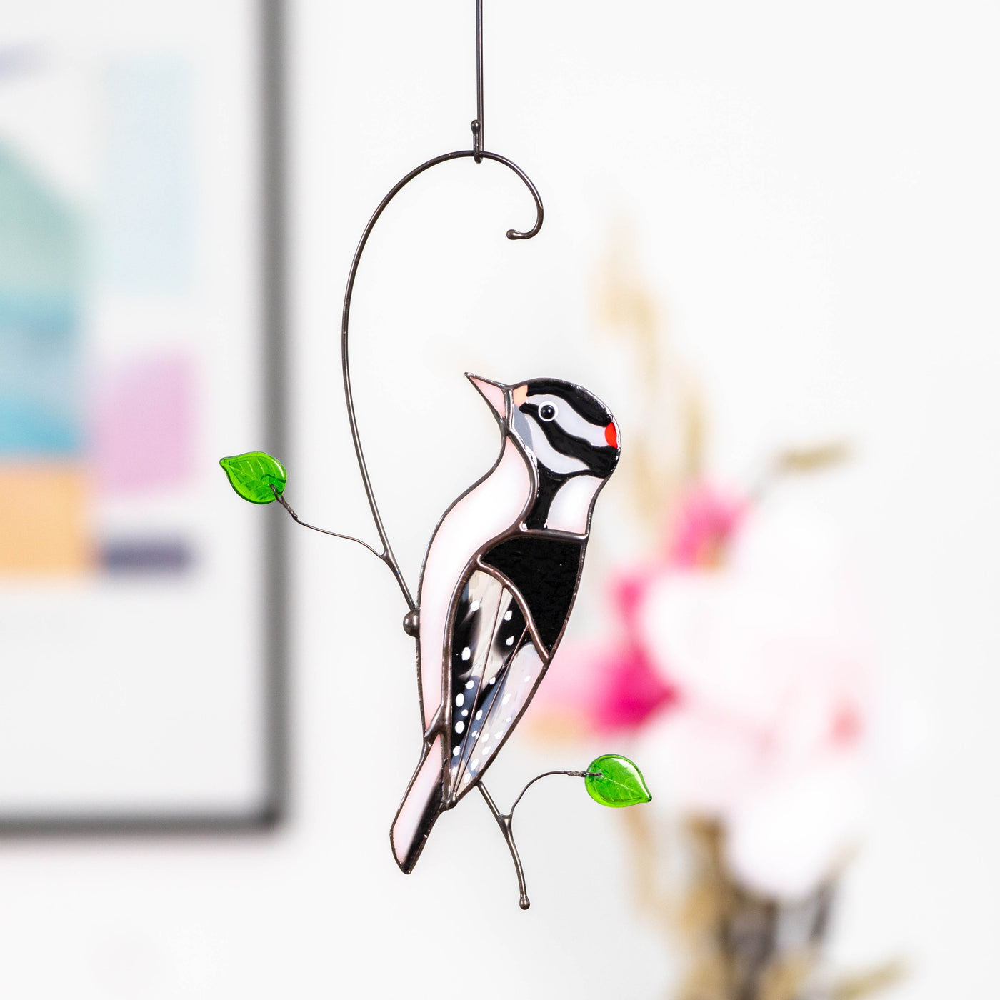 Stained glass downy woodpecker on the branch with green leaves suncatcher
