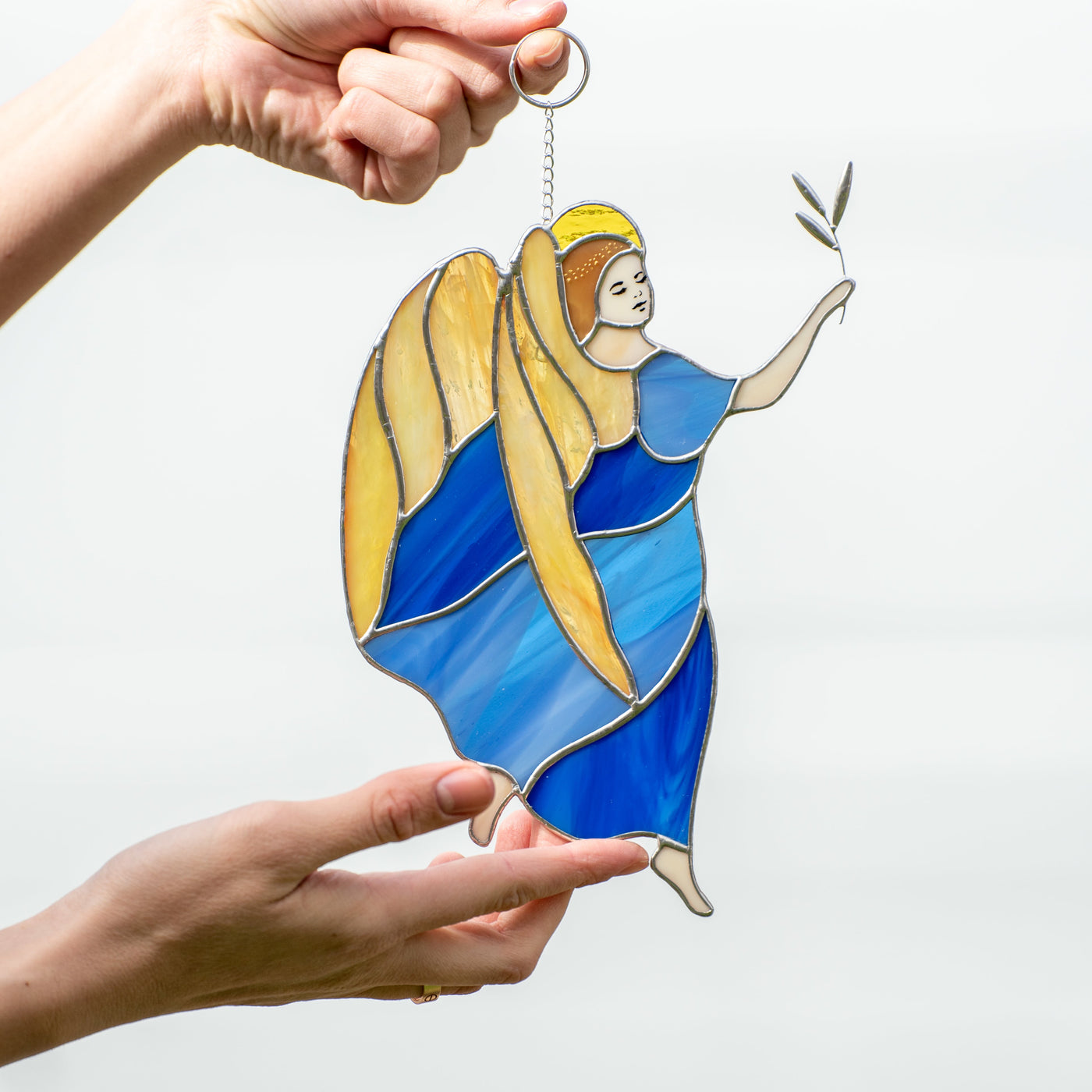 Stained glass window hanging of a guardian angel with yellow wings wearing a blue dress