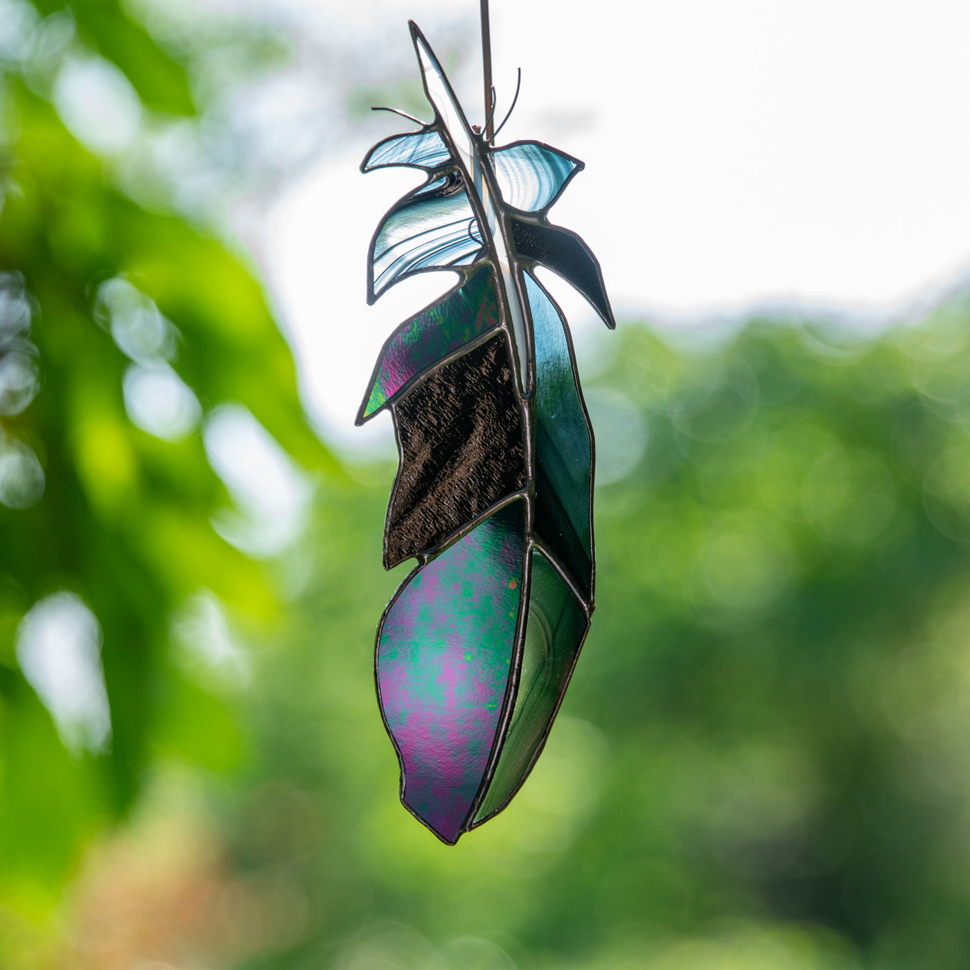 Suncatcher of a stained glass raven feather with modulating shades
