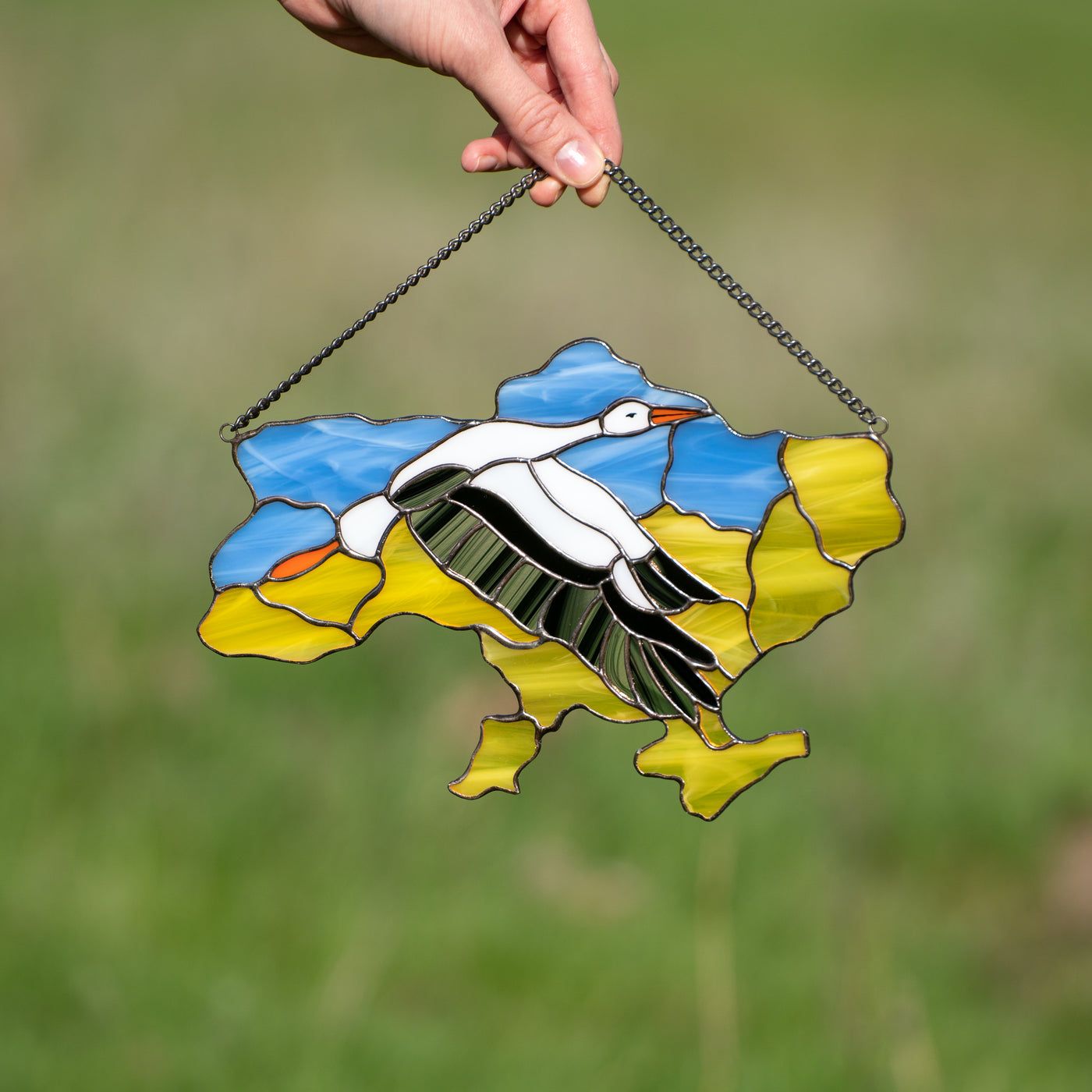 Stained glass window hanging in the shape of Ukraine depicting a flying stork in the middle