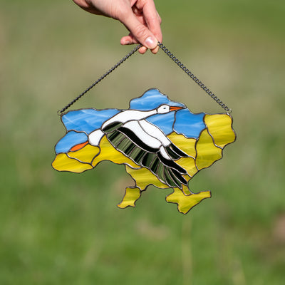 Stained glass window hanging in the shape of Ukraine depicting a flying stork in the middle