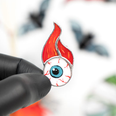Torn out eye with fire above pin of stained glass 
